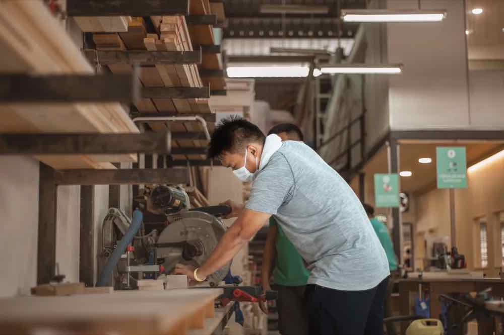 A trainee cutting a panel on a mitre saw at KitaBina