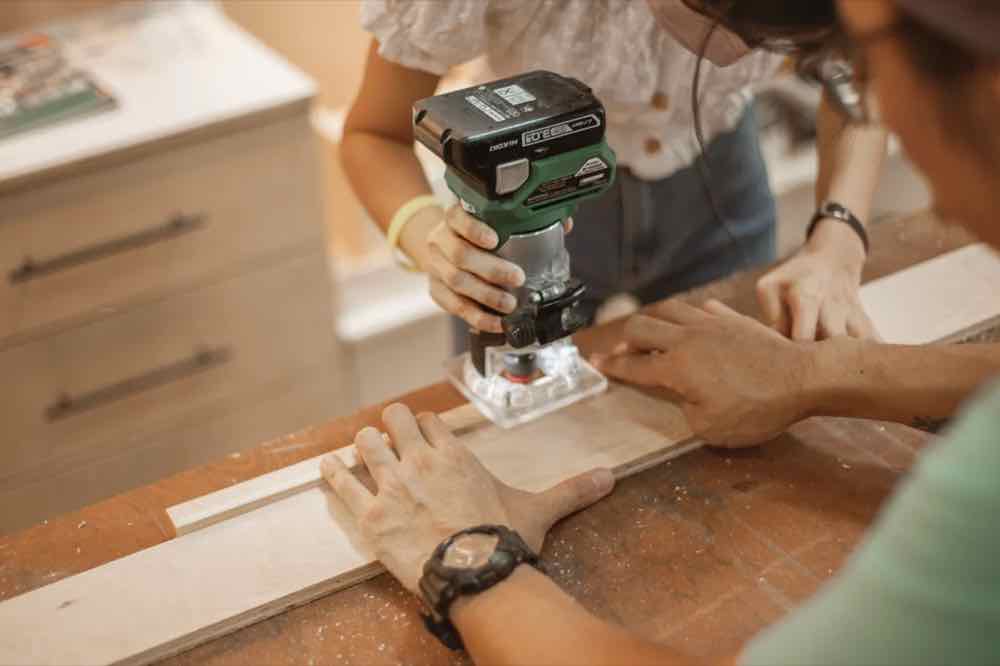 A trainee guiding a trim router along a panel edge