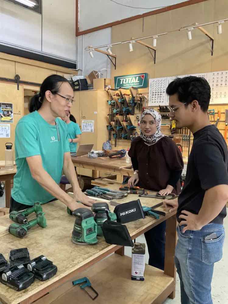 KJ demonstrating a sander to trainees at a workbench