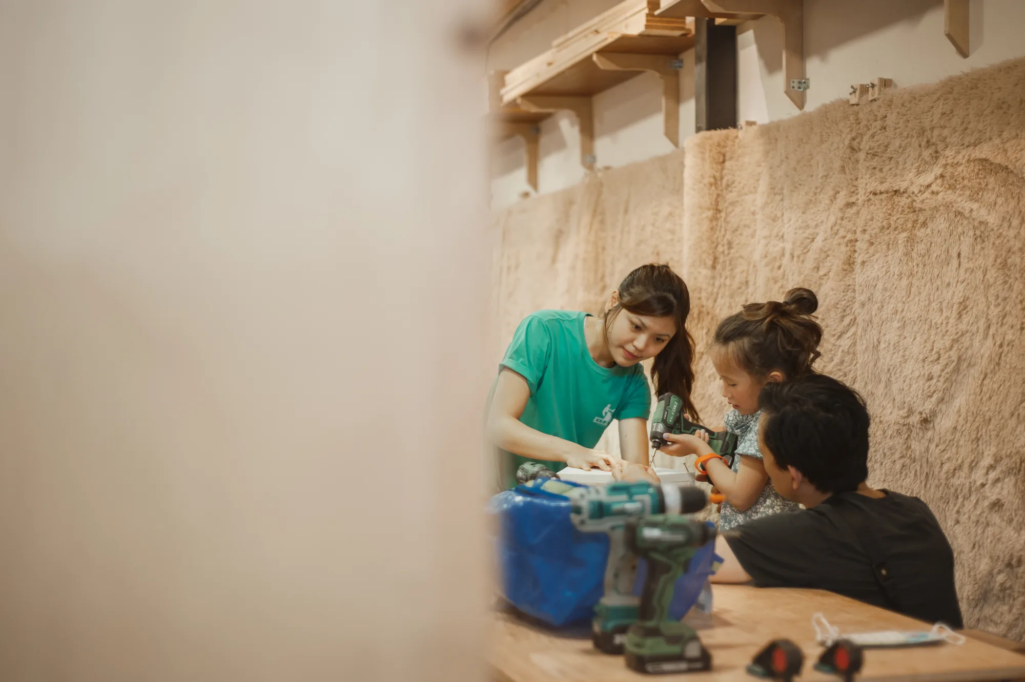 An instructor guiding two young makers through a drill at the table