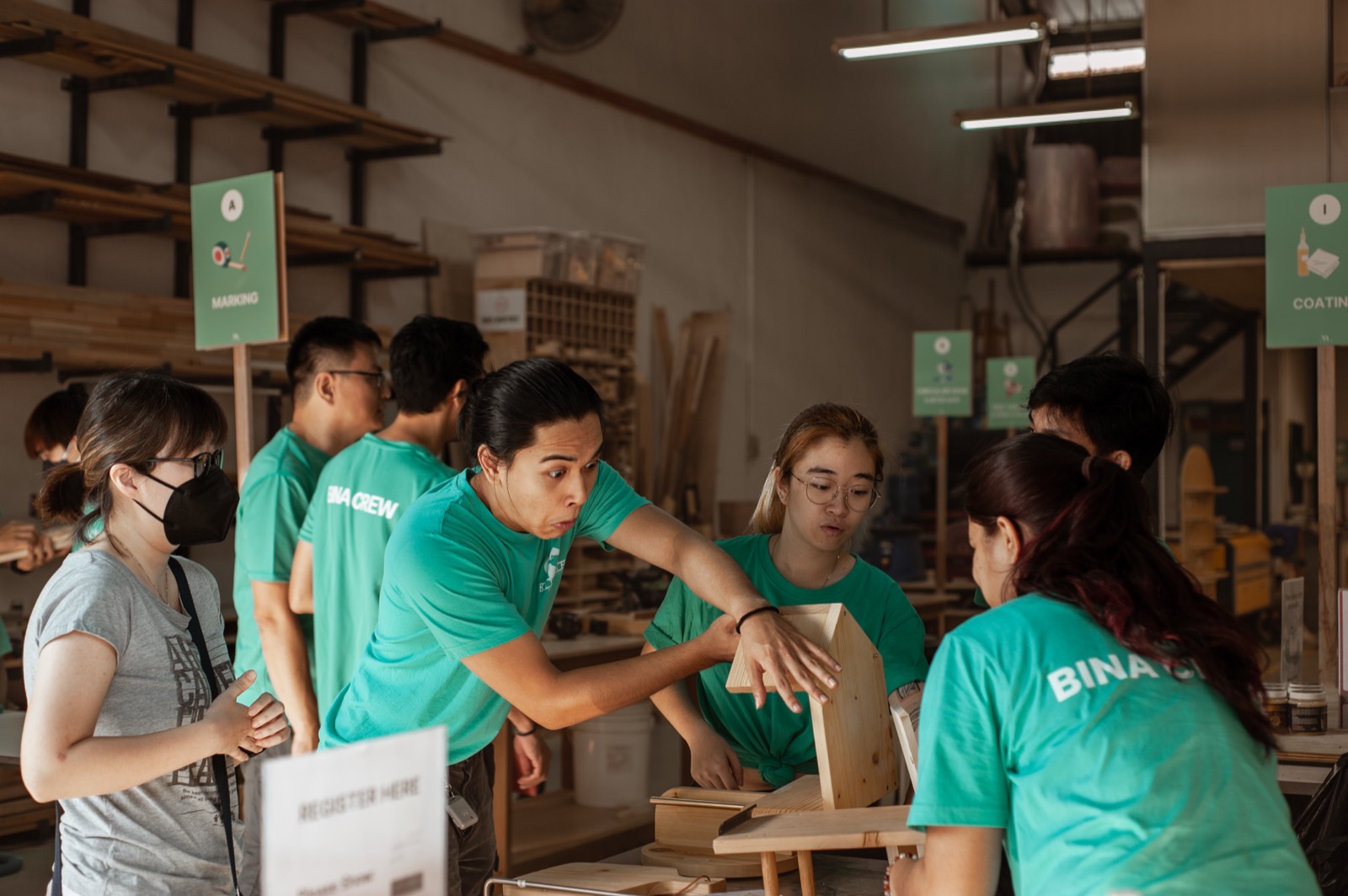 KitaBina crew in teal shirts guiding visitors through a build around a workshop table at Pesta Bina